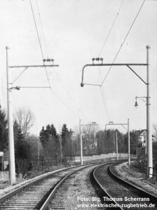 zweigleisige Strecke im Rechtsbogen mit Oberleitung an Betoneinzelmasten mit waagerechten Auslegern darauf stehenden stehenden Dreieraggregat
