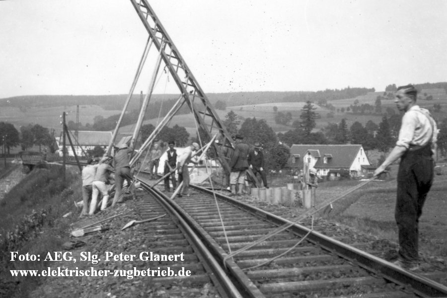 Auf freier Strecke im Bogen wird ein Mast mit Hilfe von Stangen und Seilen gestellt.